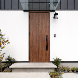 玄関アプローチ。コンクリートの無機質な感じがかっこよさを引き立てます。また、重厚感のある玄関ドア(LIXIL フォーラード)とクリアな庇、少しレトロなアイアンのポーチライトの組み合わせが目を惹きます。