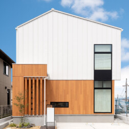 外観は、白のガルバリウムと木目調のサイディングの貼り分け。上品でナチュラルに仕上がりつつ、モダンな外壁が前を通る人の視線を釘付けです。玄関前に格子をつけることで、視線を遮る効果にもなります。